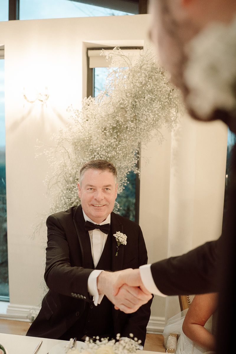 A person in a black tuxedo and bowtie shakes hands during a celebration with glitter falling from above.