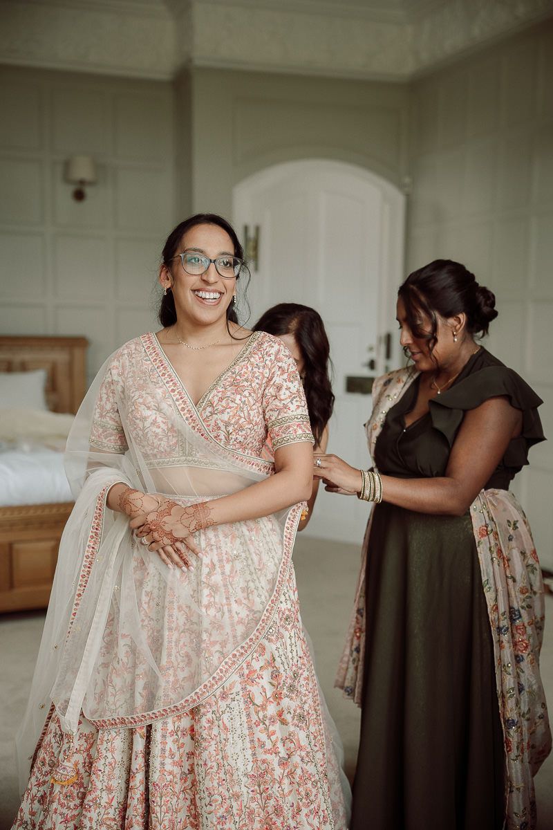A group of bridesmaids wearing elegant cream and floral dresses share candid moments together before a wedding.