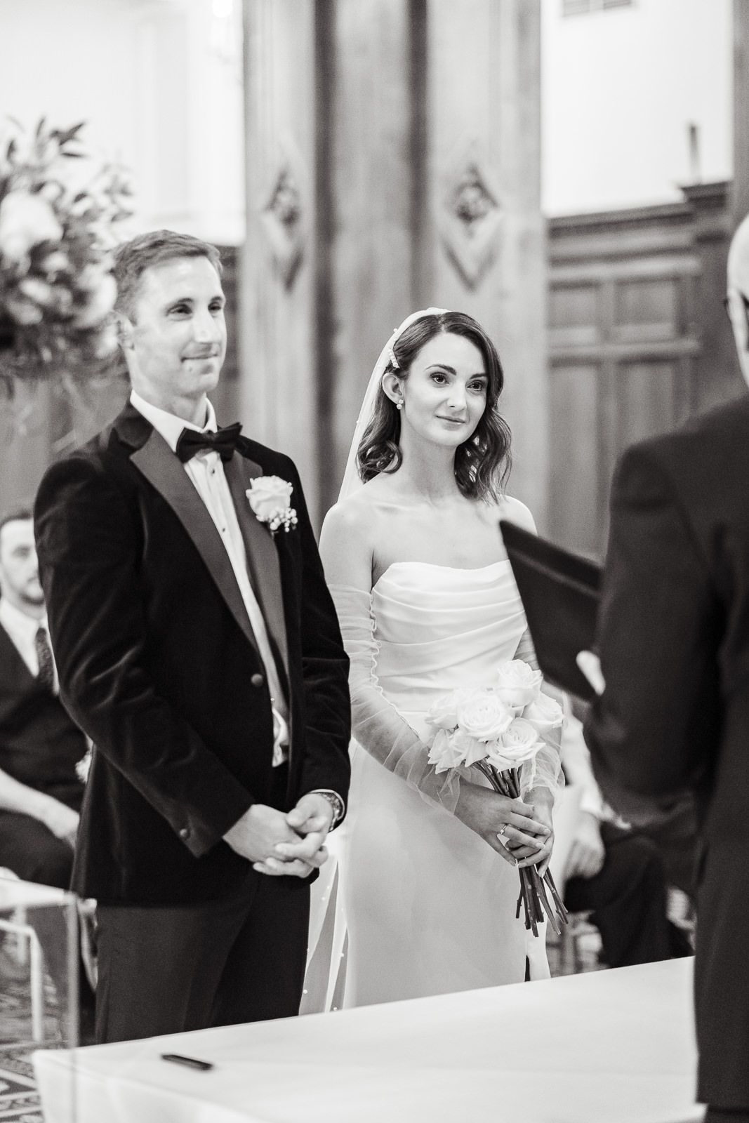 A couple in formal wedding attire stands at the altar during their ceremony in a black and white photo at intimate london wedding.