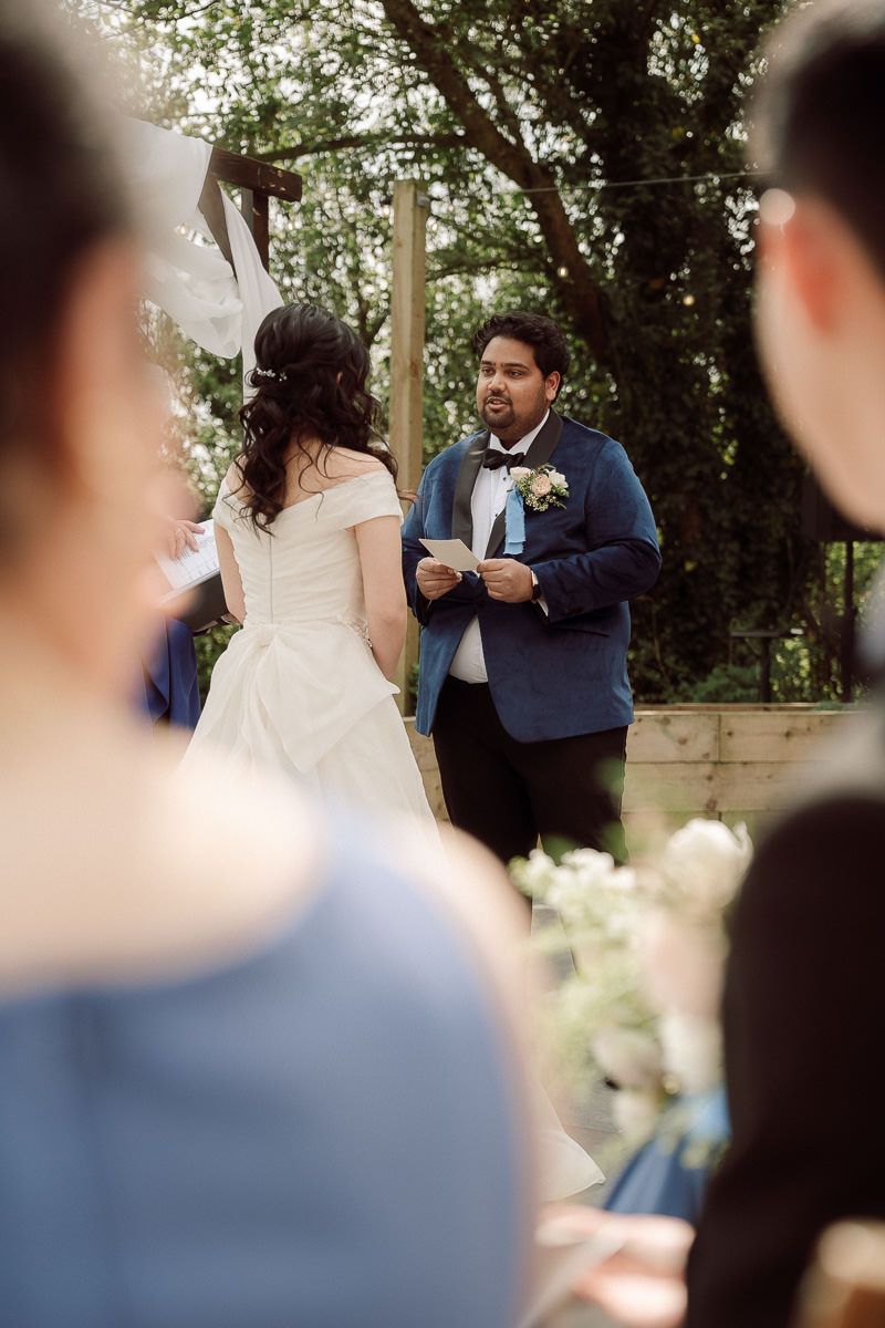 Wedding guests gather outdoors under trees during a daytime celebration.