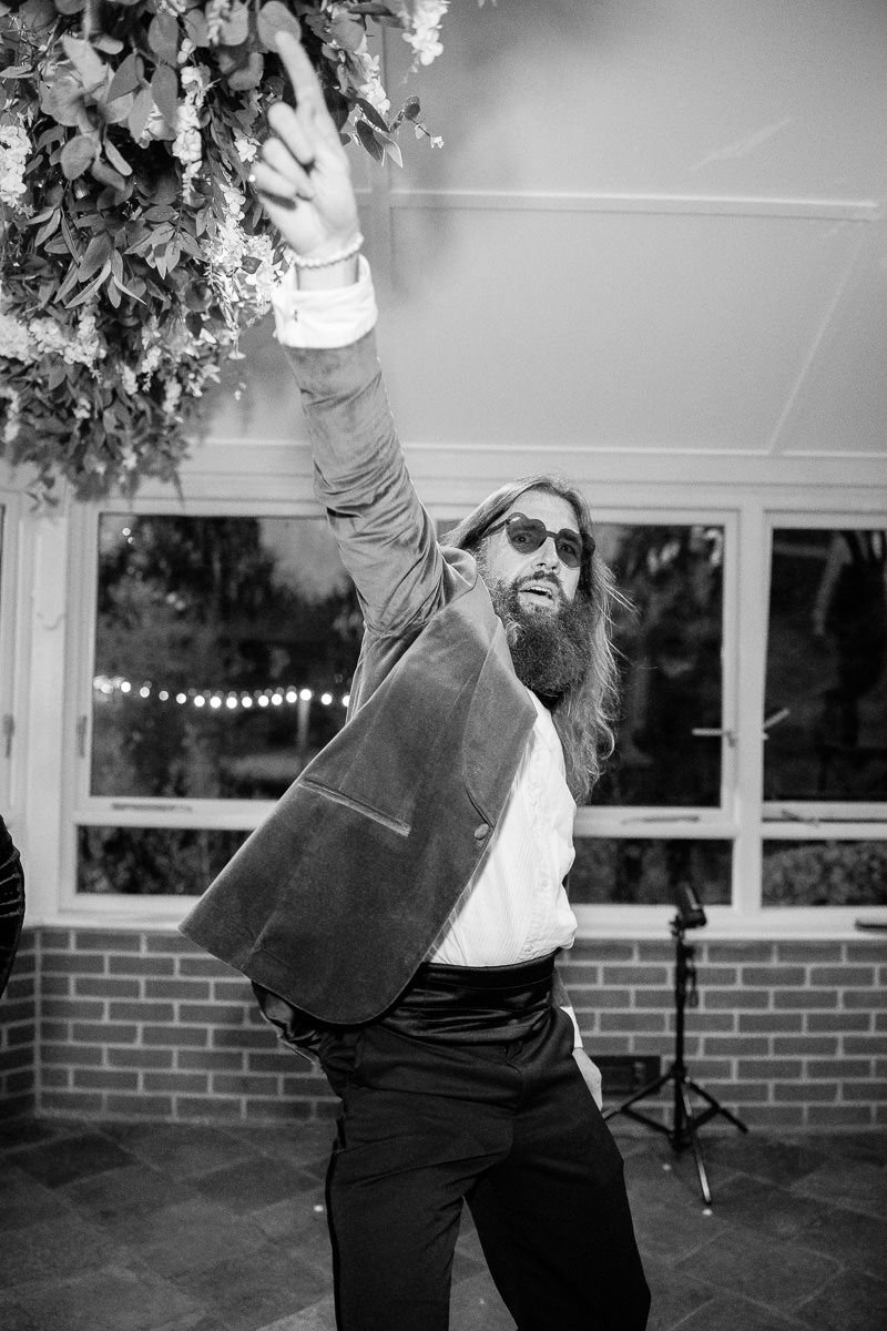 Black and white sequence showing joyful dancing at a wedding reception under string lights and floral decor.