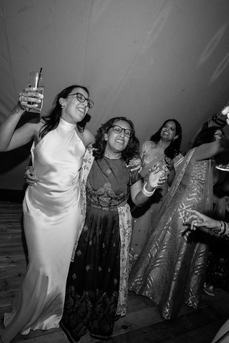 Wedding guests celebrating and raising glasses during a festive reception party in black and white.