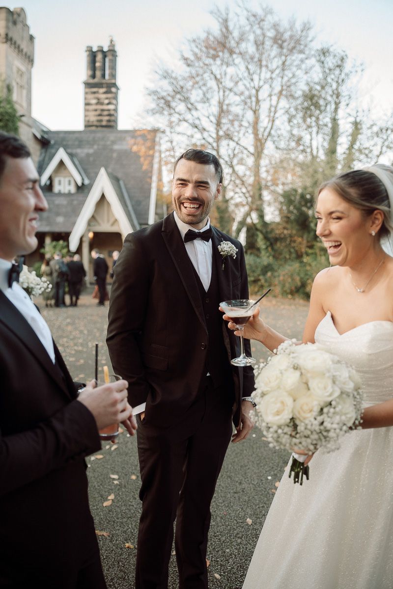 A joyful wedding couple shares a candid moment outdoors while holding a white floral bouquet.
