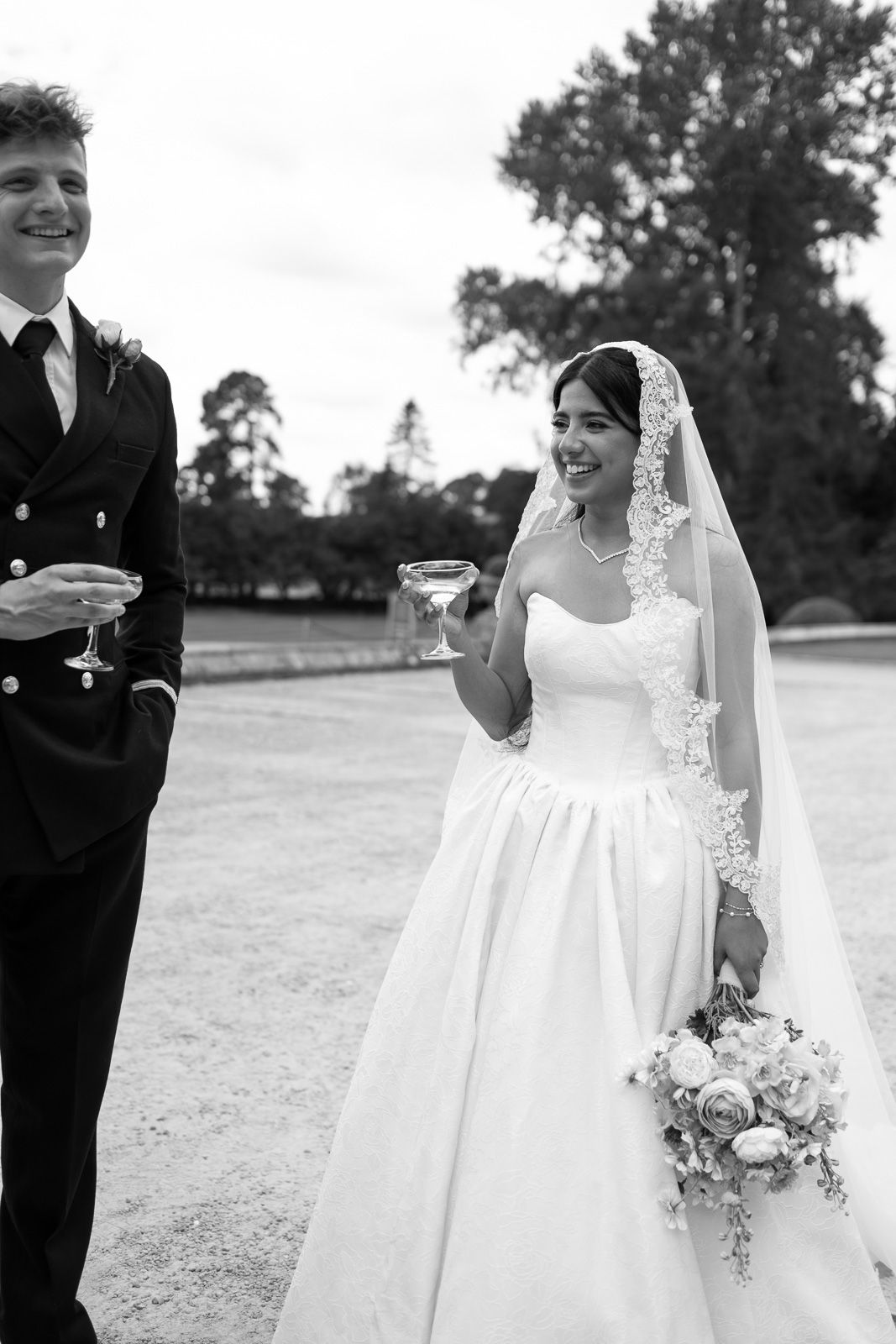 Black and white photo of smiling bride and groom toasting with champagne at outdoor wedding.