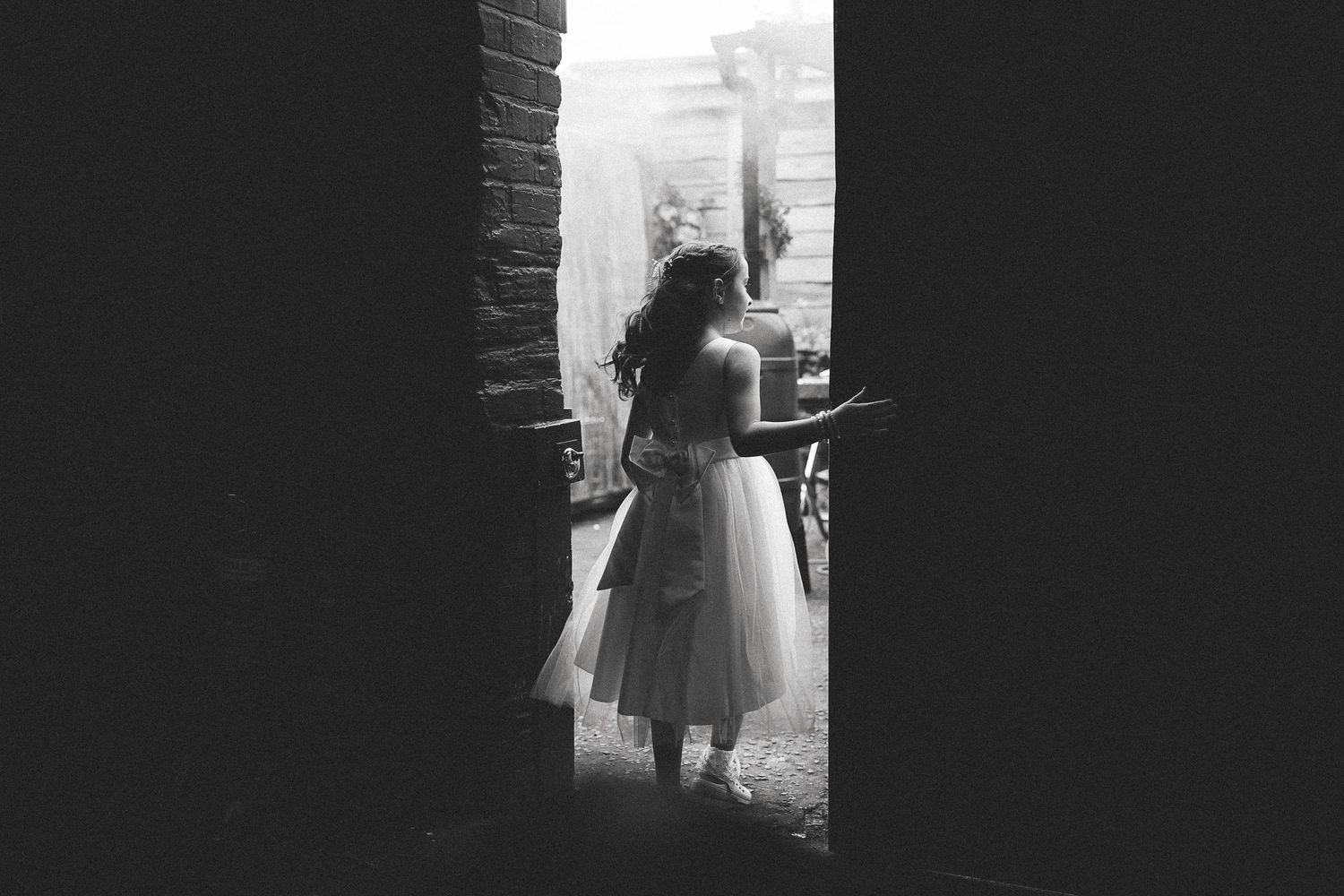 A silhouette of a person in a dress stands by a window in a black and white photograph.