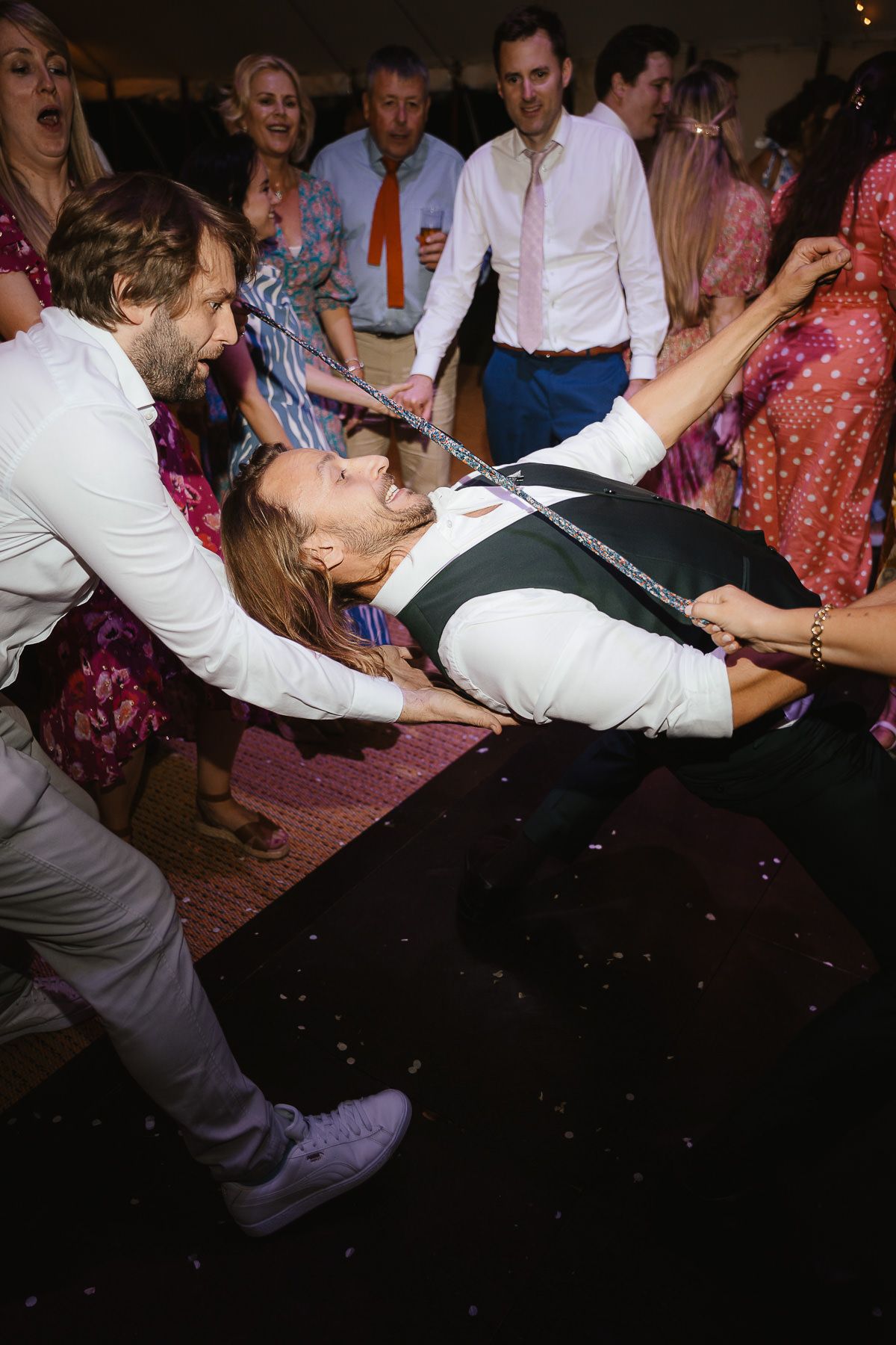 People dancing at a wedding reception with dynamic movement and enthusiasm visible on a dark dance floor.