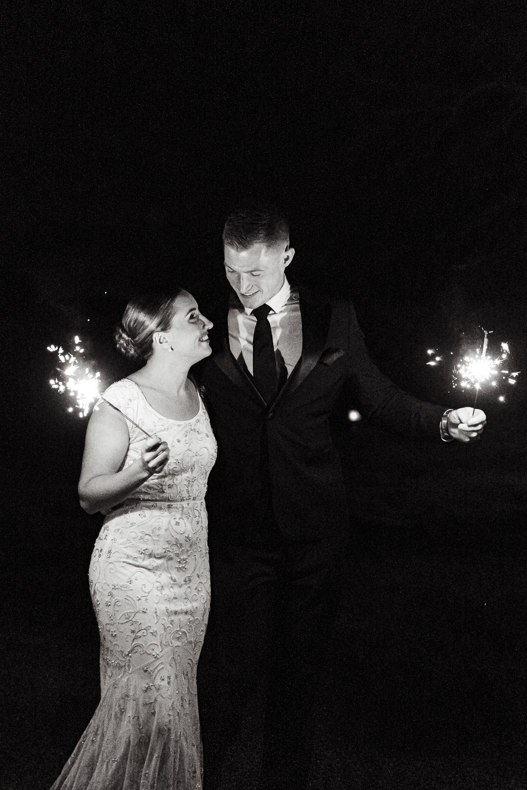 Couple shares a romantic moment holding sparklers at night in black and white wedding photography.