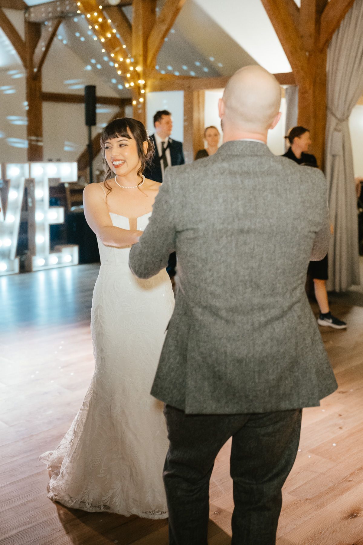 A couple dances together at their wedding reception under twinkling fairy lights in a rustic venue setting.