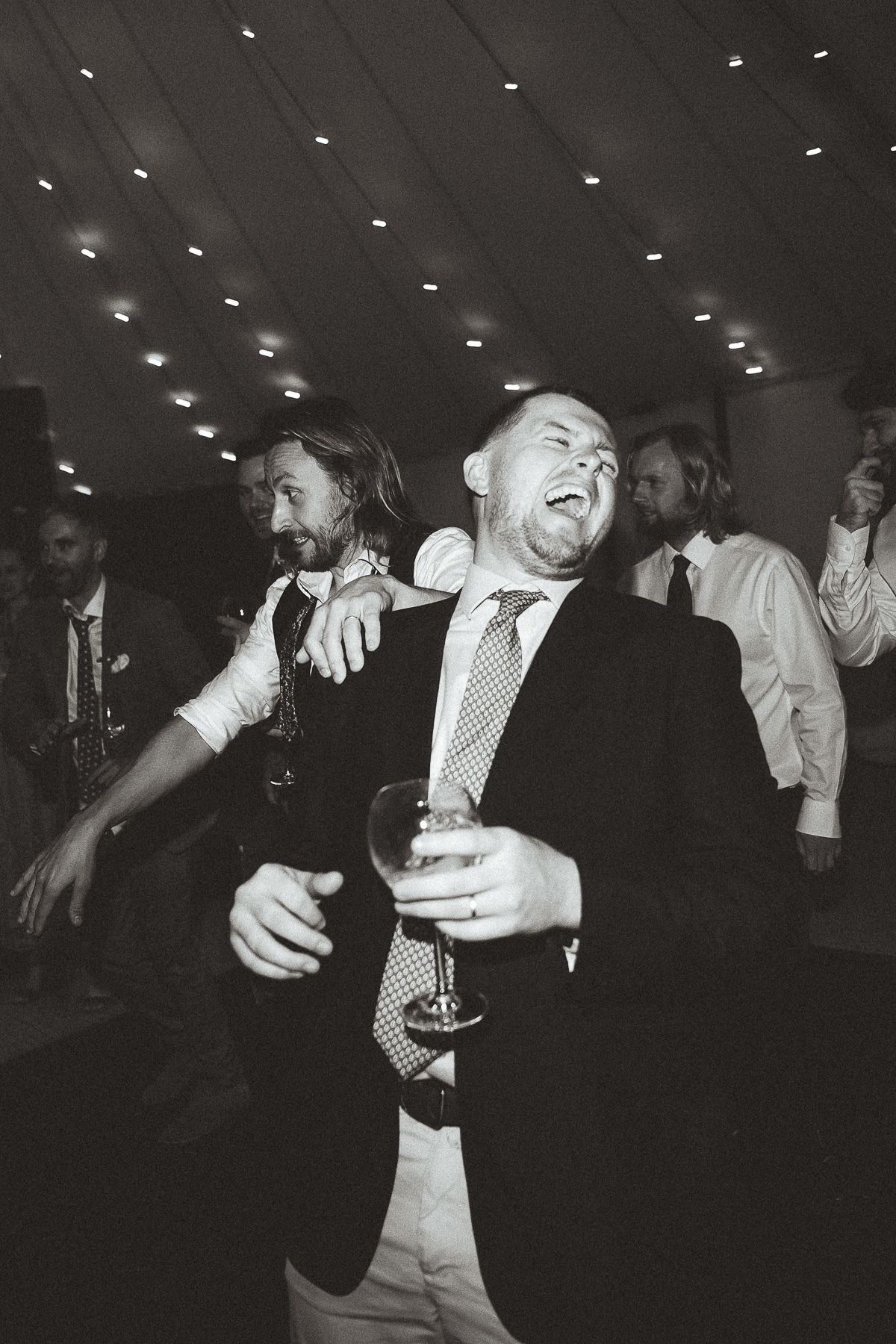 Black and white photo of wedding party guests dancing and celebrating on the dance floor at a reception.