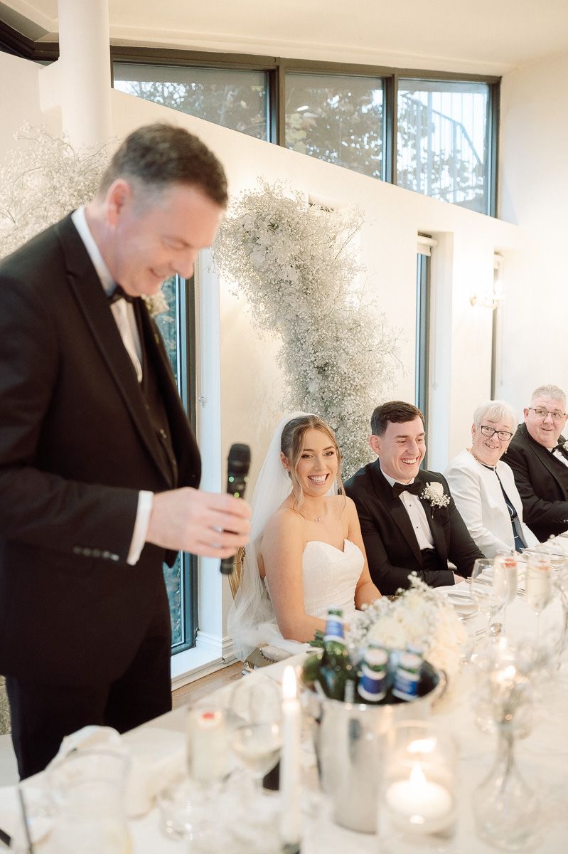 Wedding reception guests seated at an elegant white table with candles and decorative elements during dinner service.