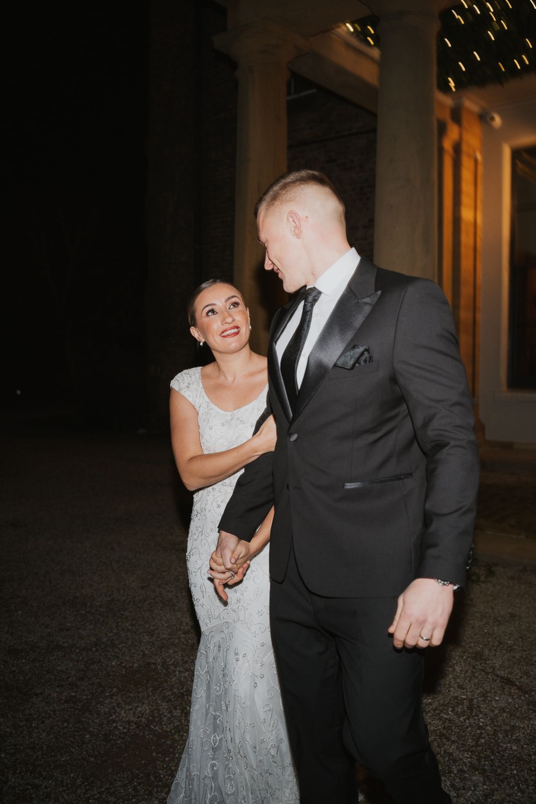 A couple shares a joyful moment together at night, with the bride wearing a sparkly white gown and groom in black suit.