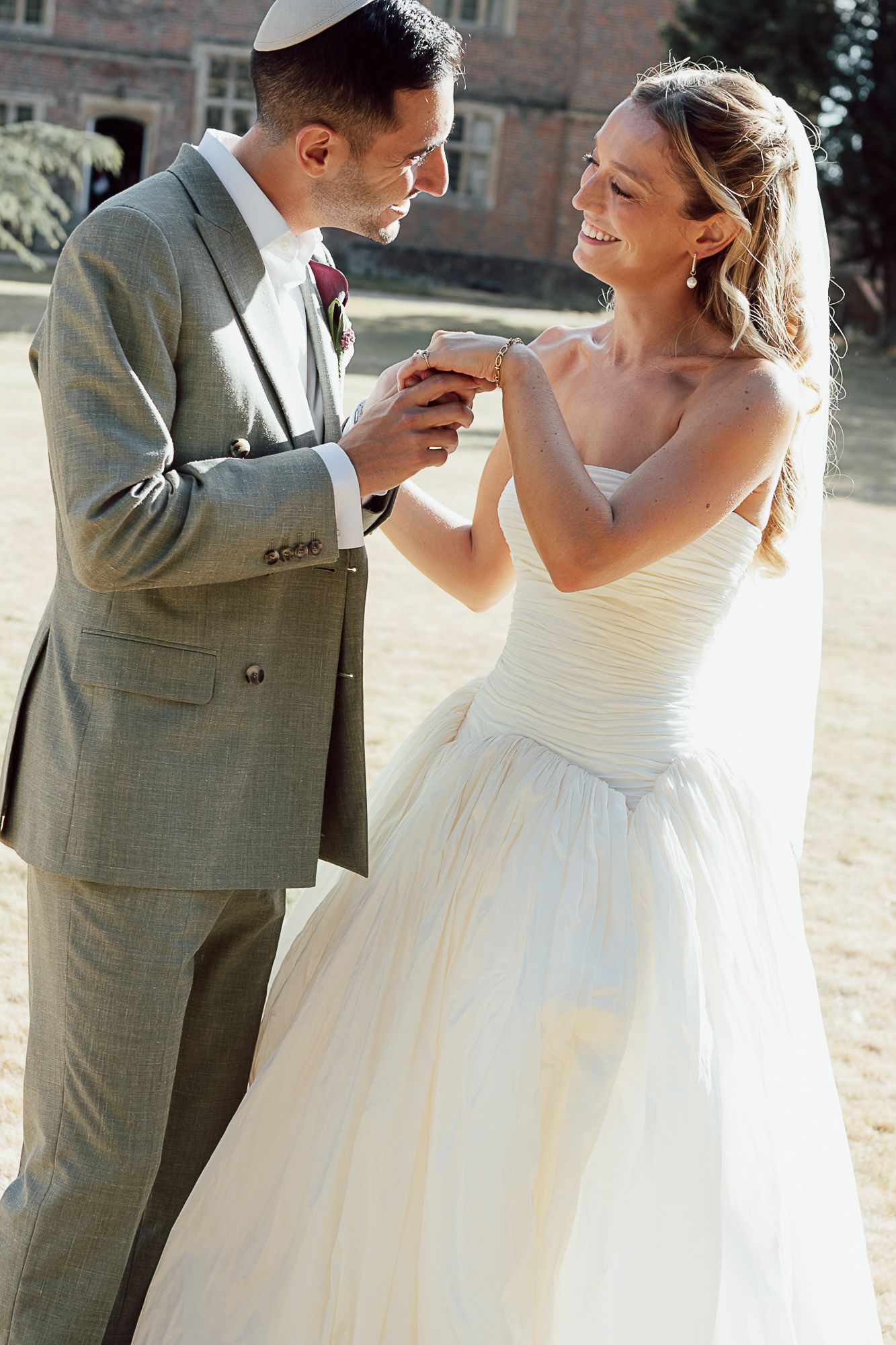 Bride and groom exchanging rings outdoors, smiling joyfully in wedding attire on a sunny day.