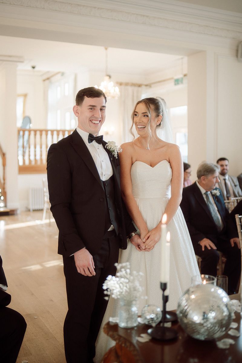 A joyful wedding ceremony moment captured in a bright, elegant white chapel setting with decorative glass centerpieces.