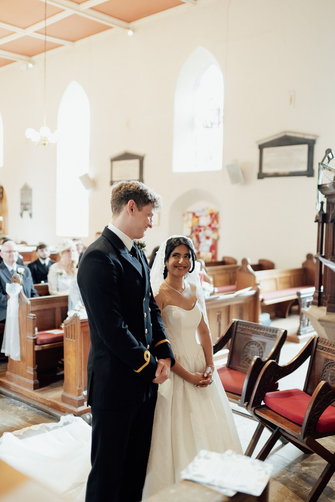 Bride and groom standing at church altar during wedding ceremony, bride in white gown, groom in dark military uniform.