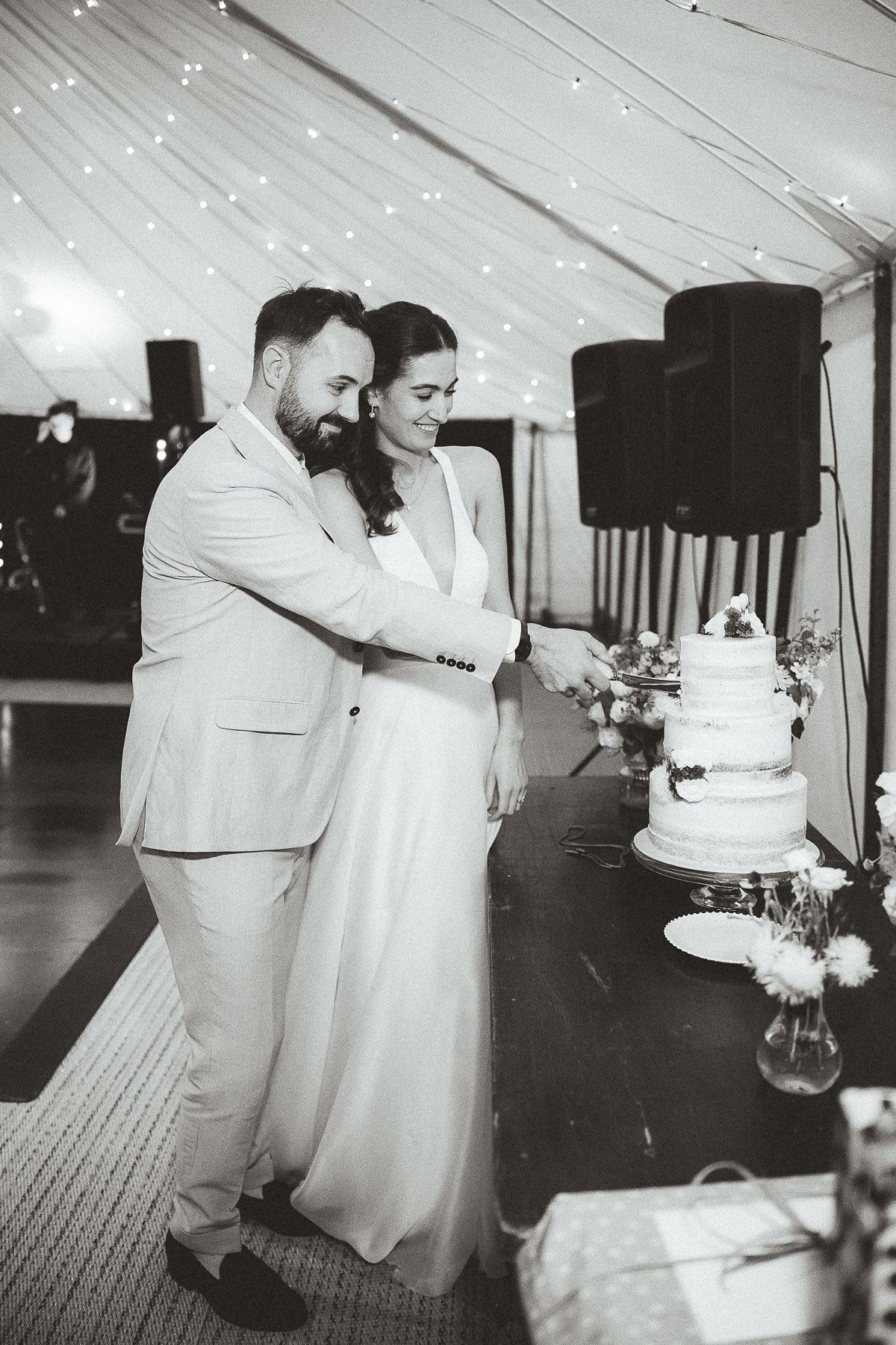 Happy couple in elegant wedding attire cutting their white tiered wedding cake together at their reception.
