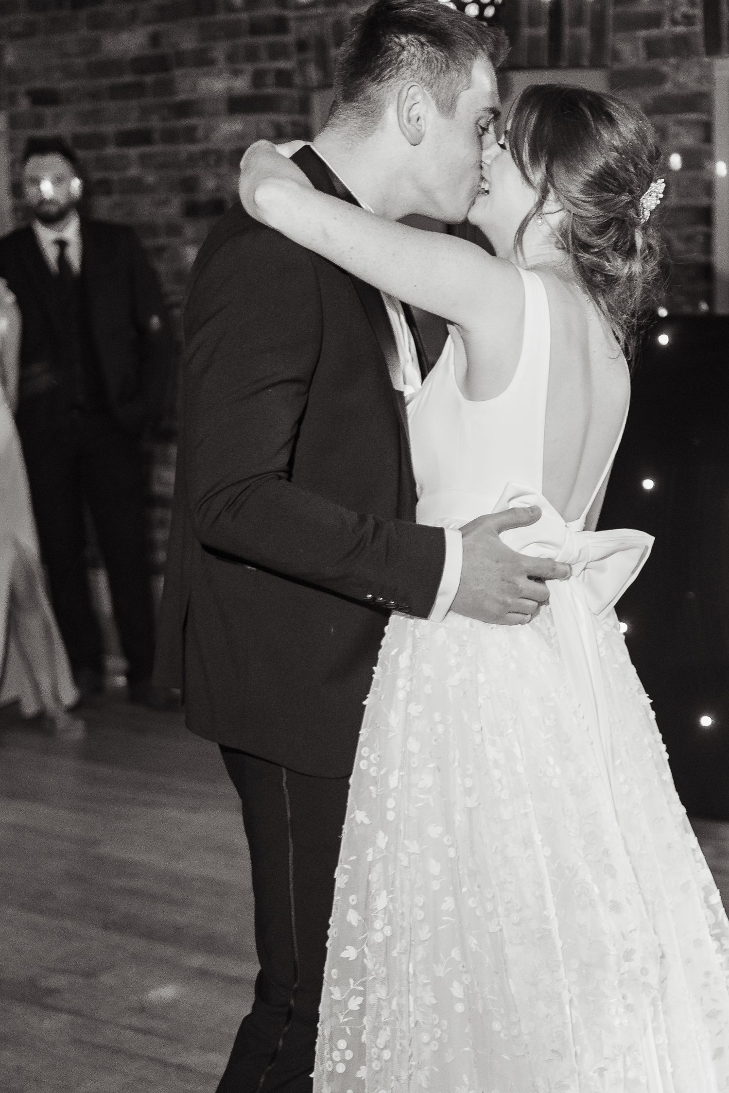 A tender first dance moment at a wedding reception with brick walls and twinkling lights in the background  at Larkspur Lodge