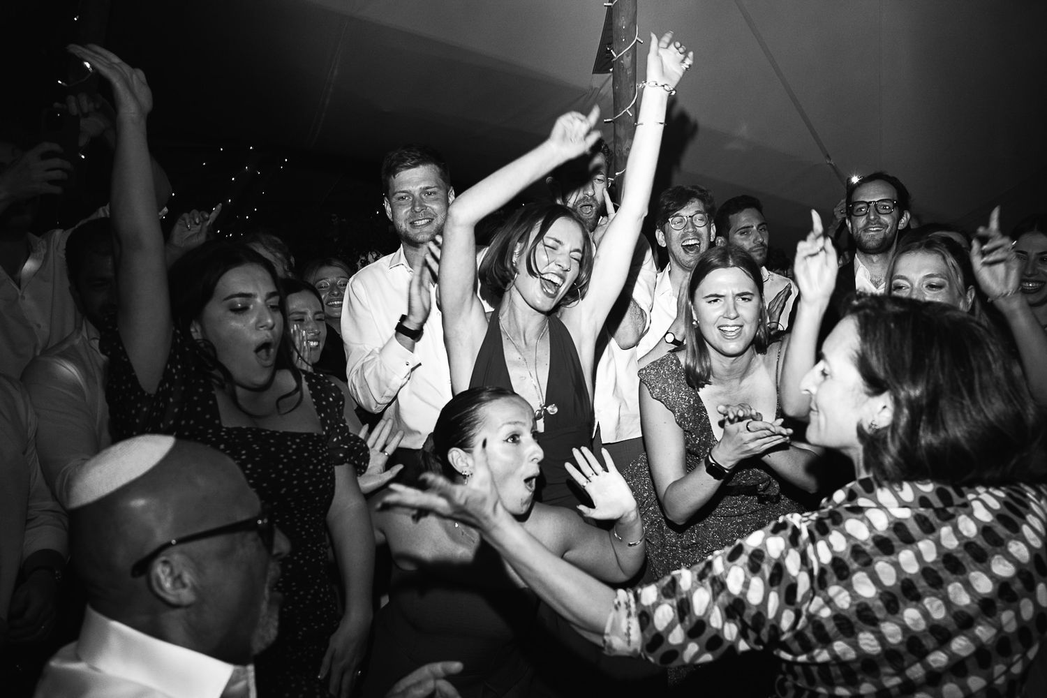 Lively black and white photo of a crowd of people dancing and celebrating at an outdoor party event.