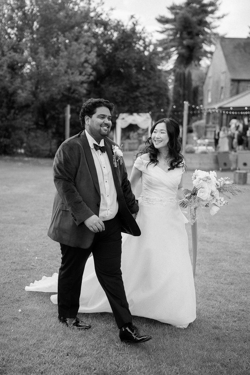 A newlywed couple laughs together on their wedding day in a garden setting at the Old Mill at Aldermaston