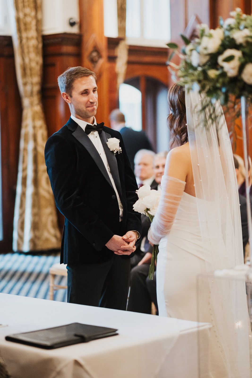 Elegant couple exchanging vows during wedding ceremony in classic church interior with floral arrangements.