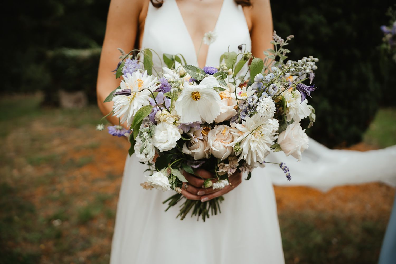 A romantic bridal bouquet featuring white calla lilies, pale purple flowers and silvery greenery against a white gown.