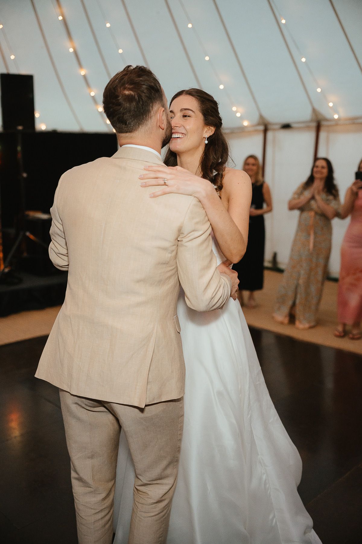A couple shares an intimate dance moment under twinkling lights at their wedding reception.