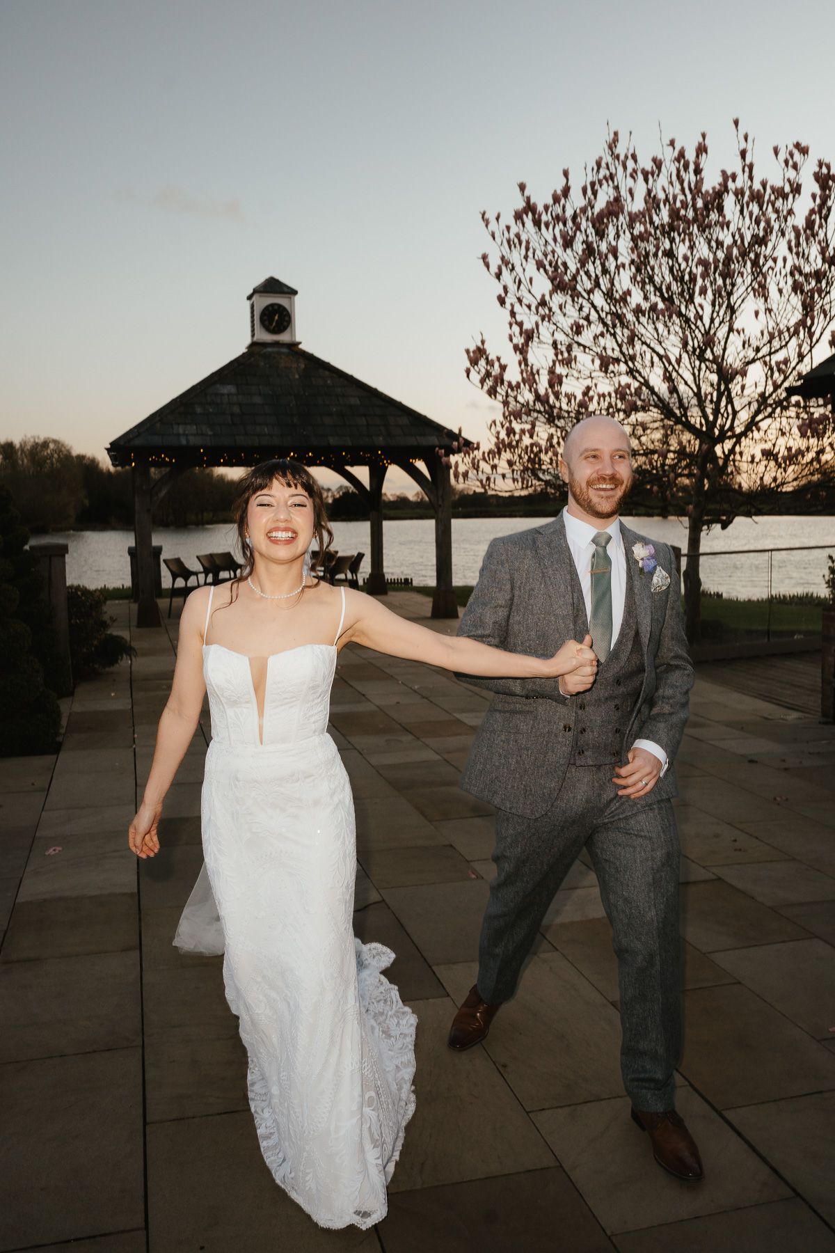 A bride and groom share a playful dance moment at sunset near a gazebo during their wedding celebration.