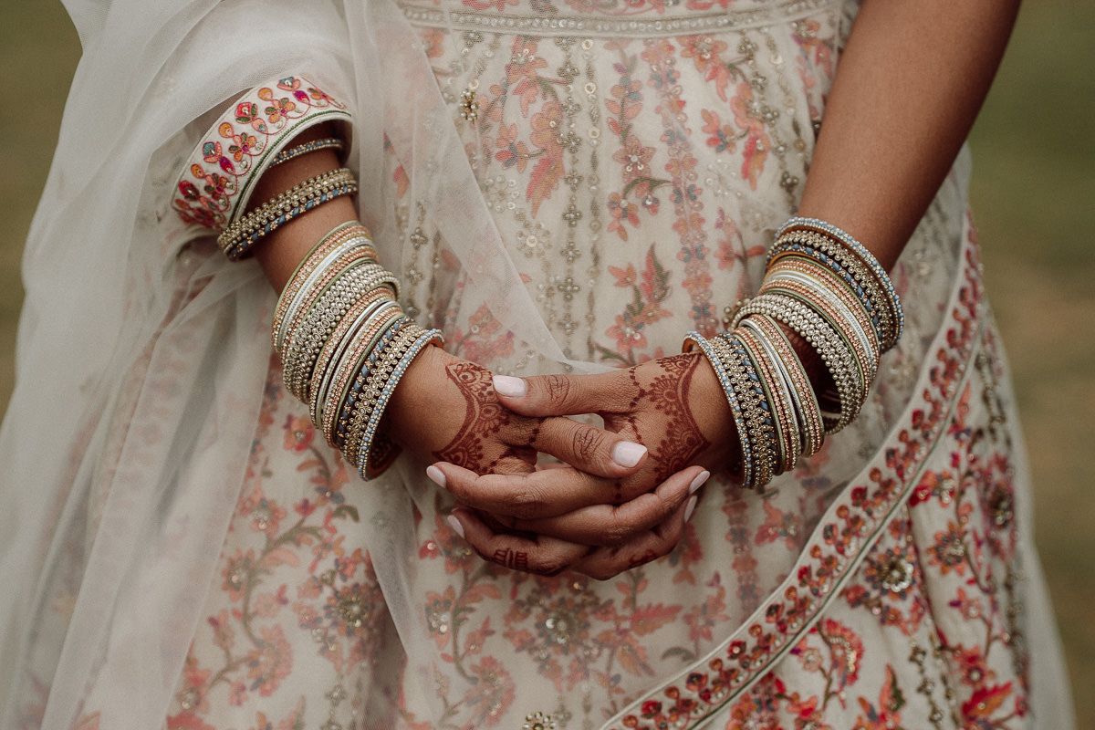 Close-up of hands adorned with traditional Indian wedding bangles and jewelry against an embroidered dress.