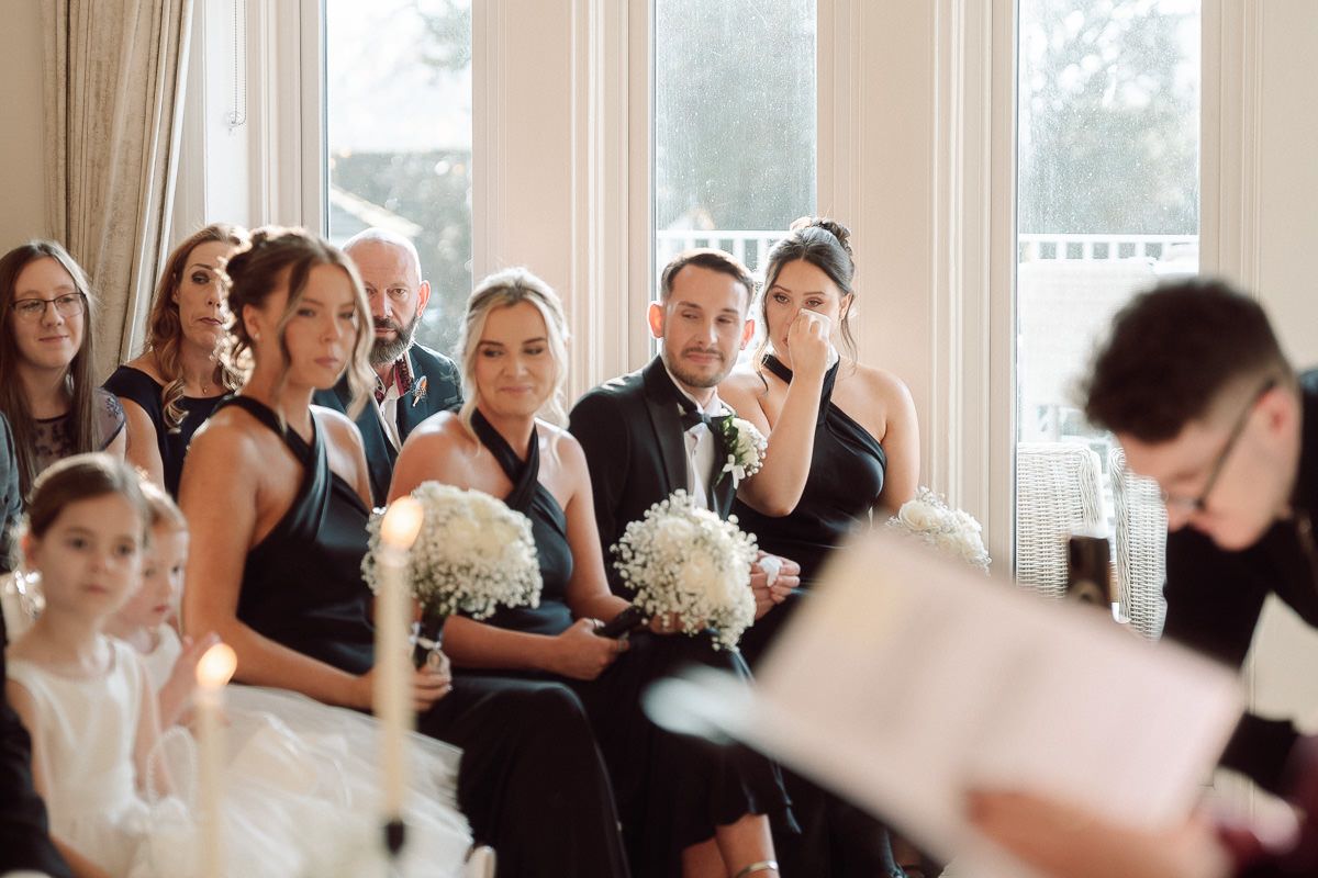Wedding guests react with emotion during a touching ceremony moment in a bright sunlit venue.