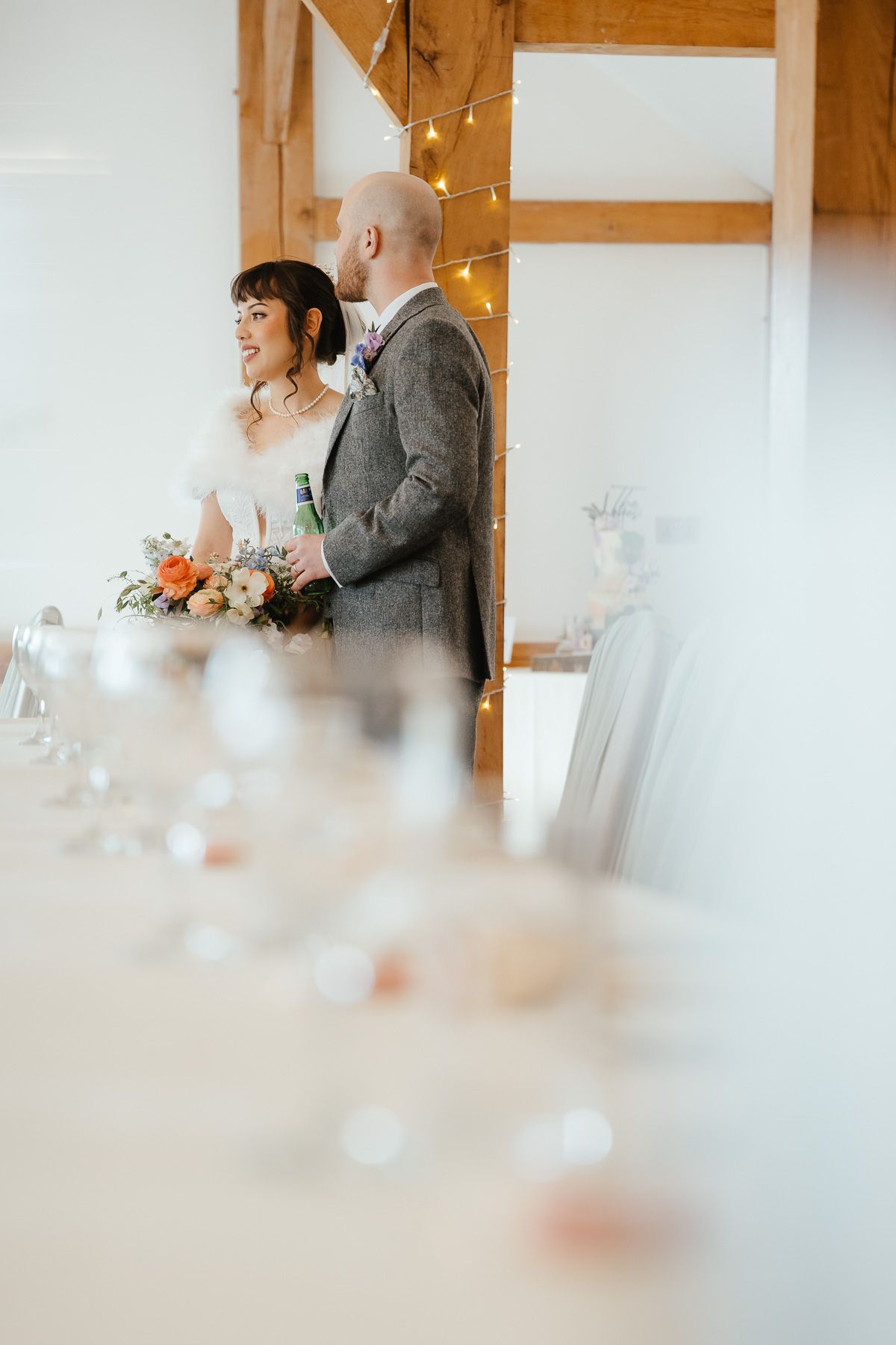 A wedding couple sharing a joyful moment in a rustic indoor reception venue decorated with string lights.