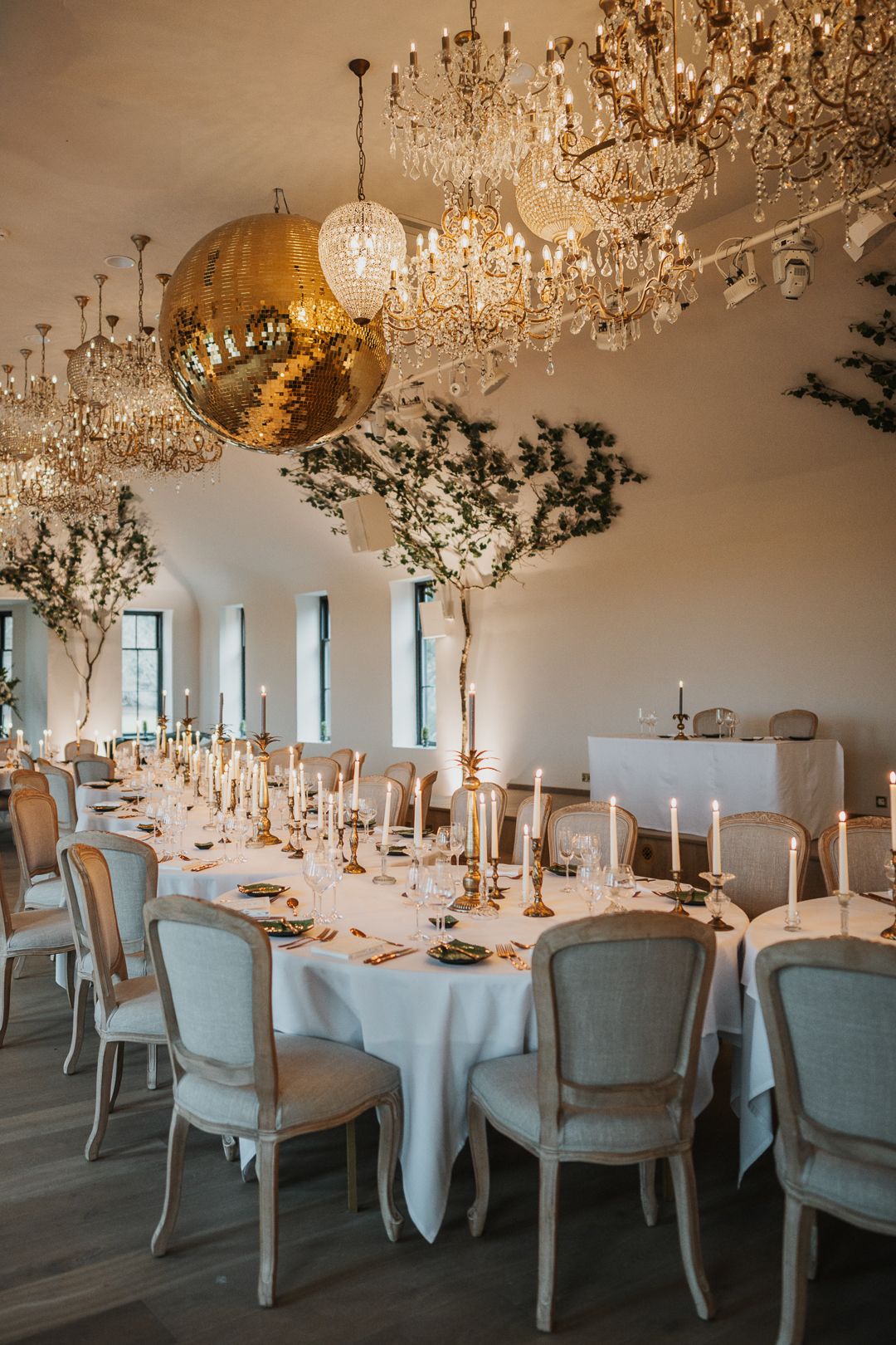 Elegant wedding reception tables set with white linens and crystal chandeliers in an upscale venue.