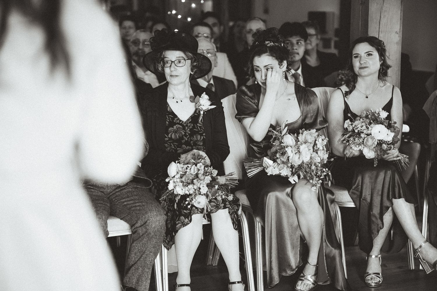 Black and white wedding party photos showing bridesmaids in elegant dresses holding floral bouquets in an indoor setting.