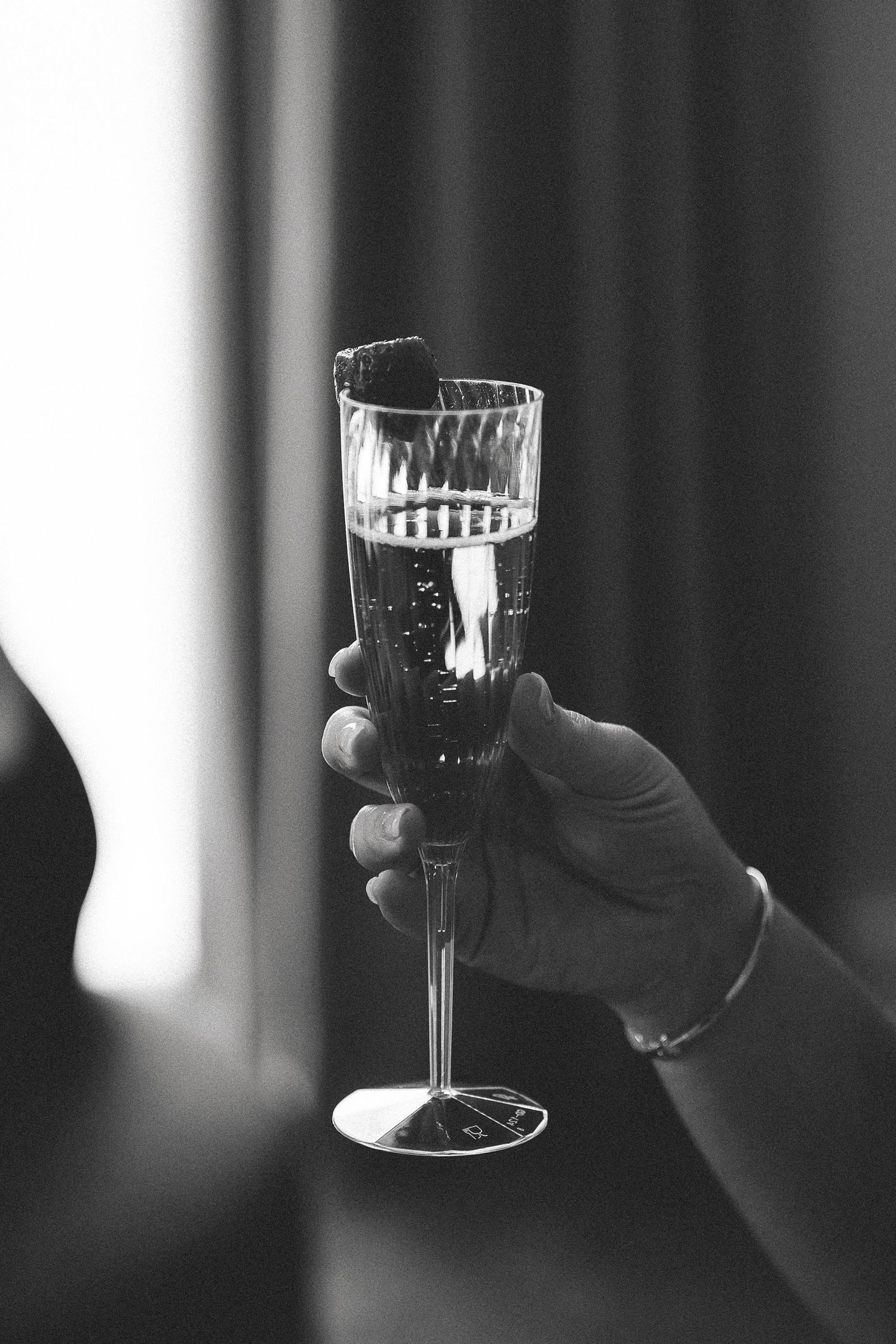 A black and white photo series showing crystal wine glasses being held up in a celebratory toast motion.