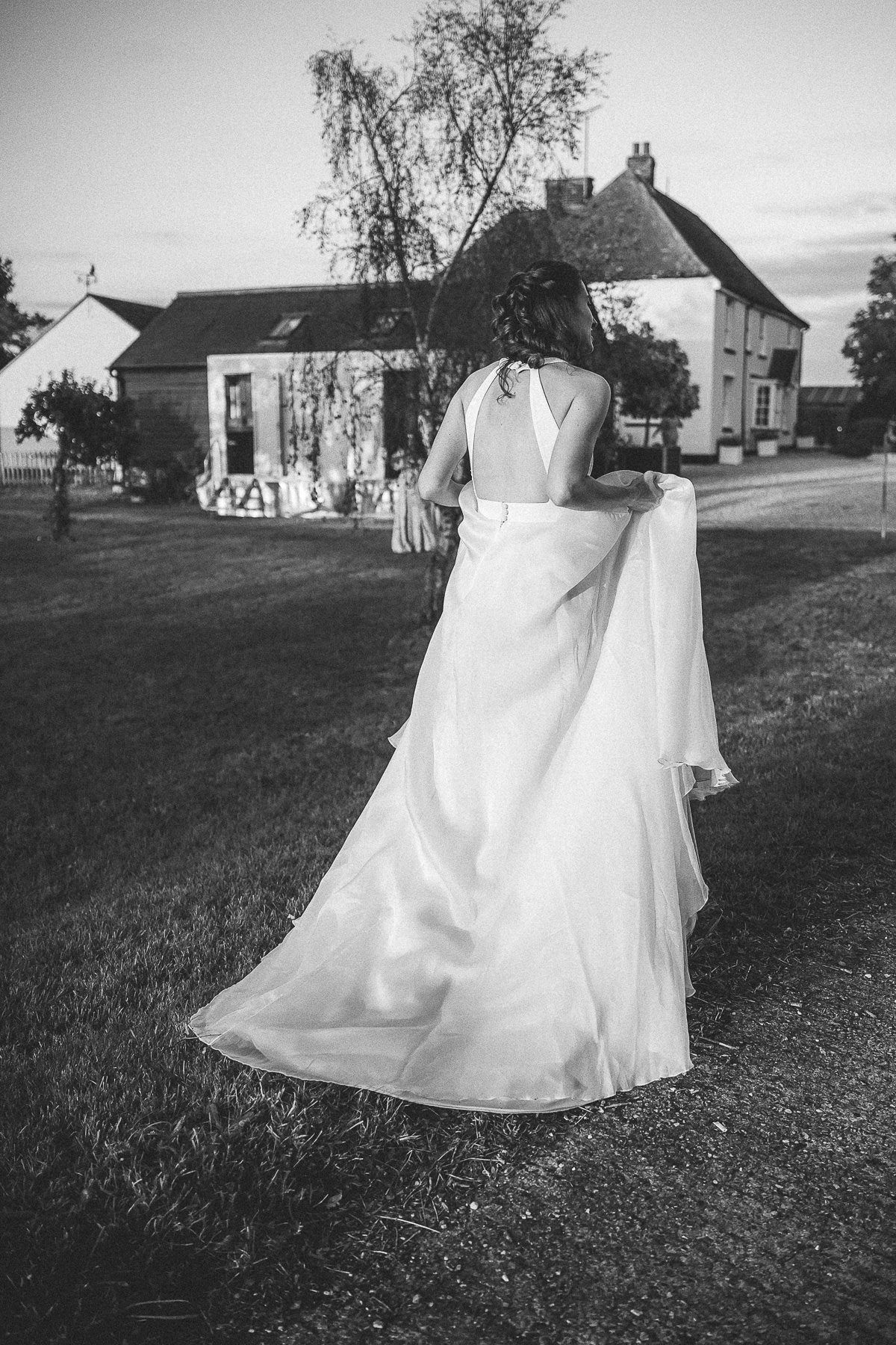 A black and white wedding photo showing a flowing white bridal gown against a countryside house backdrop.
