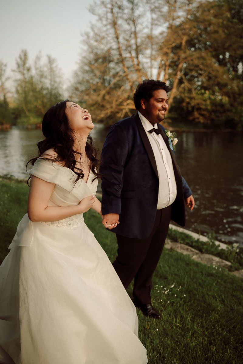A newlywed couple laughs together during their outdoor wedding photoshoot near a scenic lake.