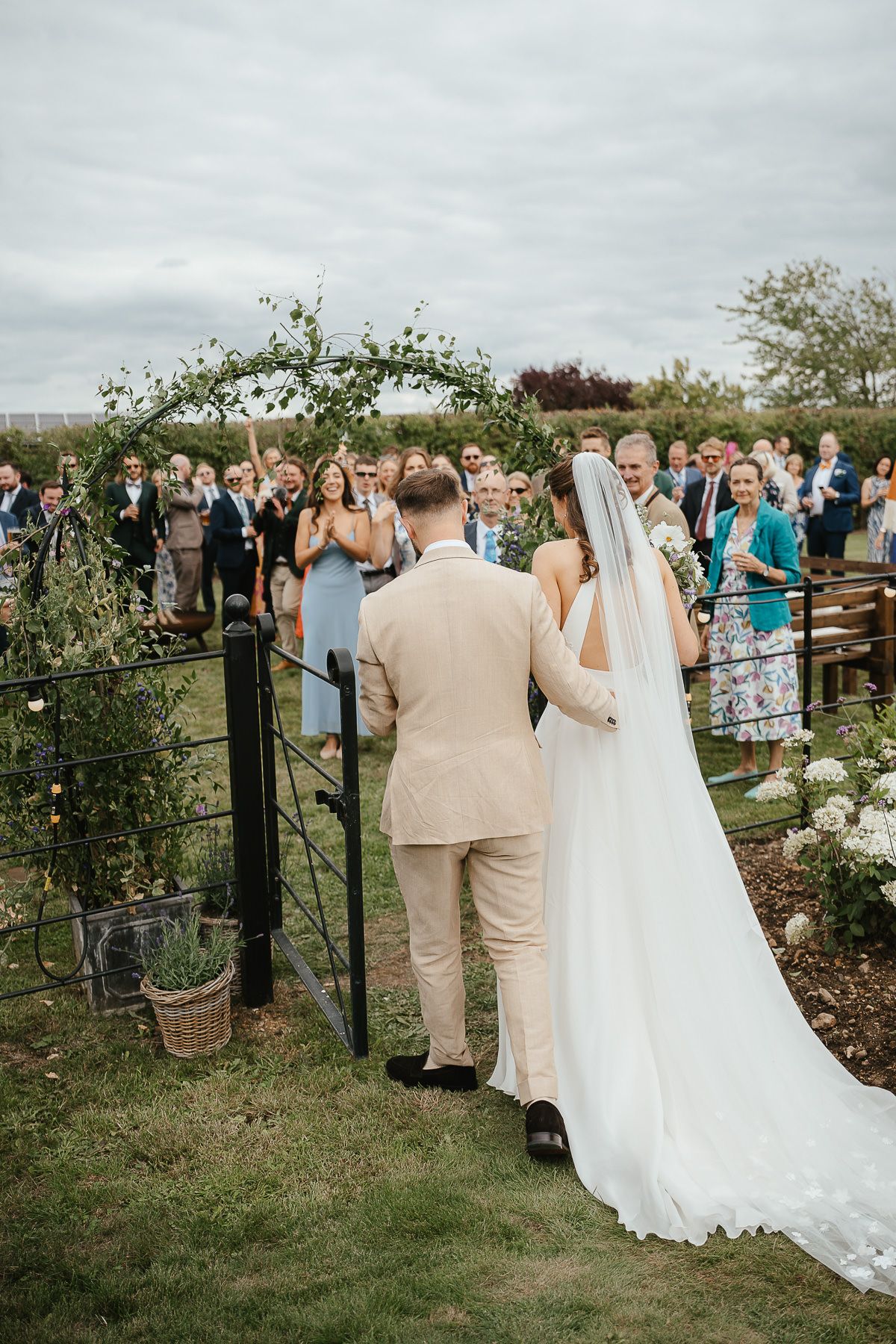 An outdoor wedding ceremony under a floral arch with guests gathered around watching the couple exchange vows.