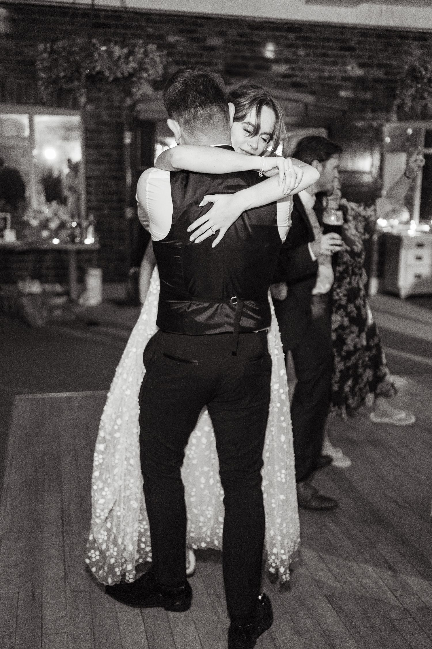 A couple shares an intimate slow dance at a wedding reception, photographed in elegant black and white on a wooden dance floor.