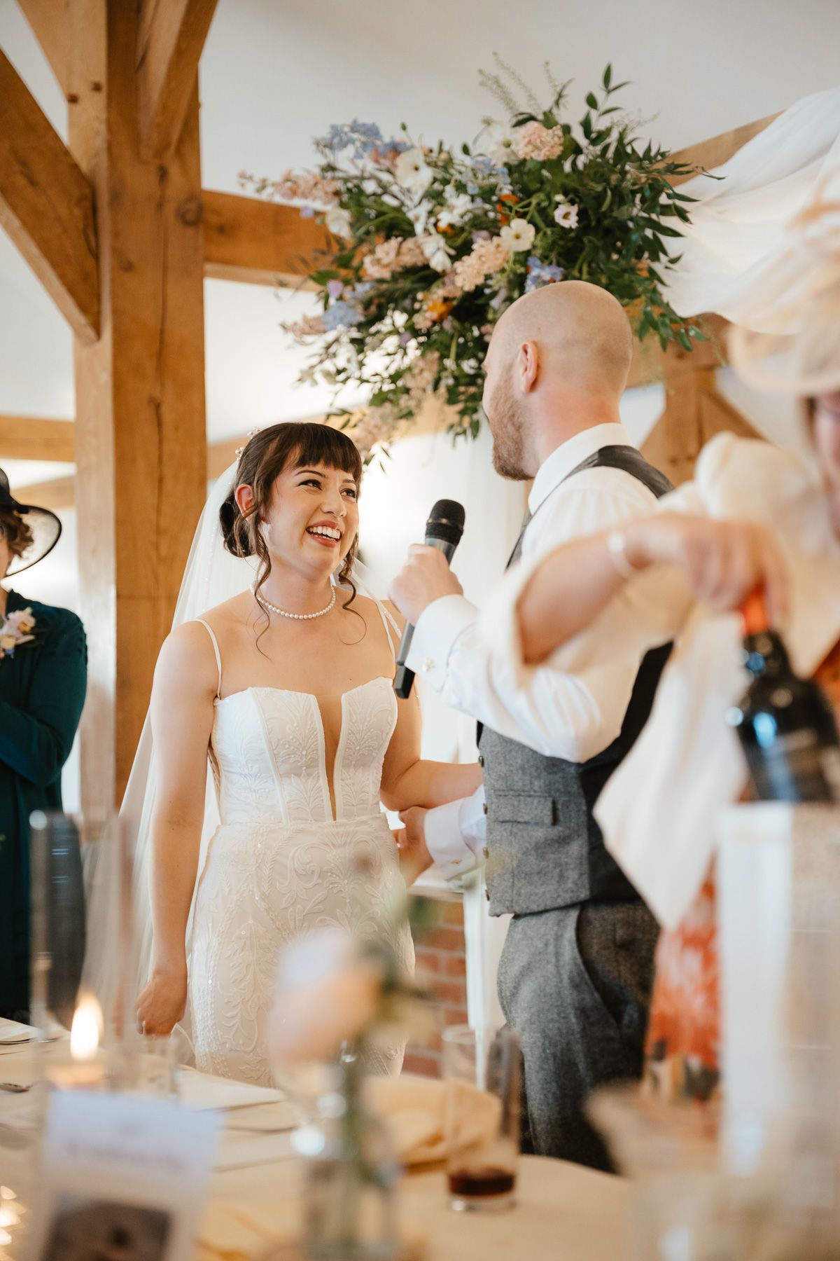 A couple share a happy moment together during a wedding reception in a rustic timber-frame venue with floral decorations.