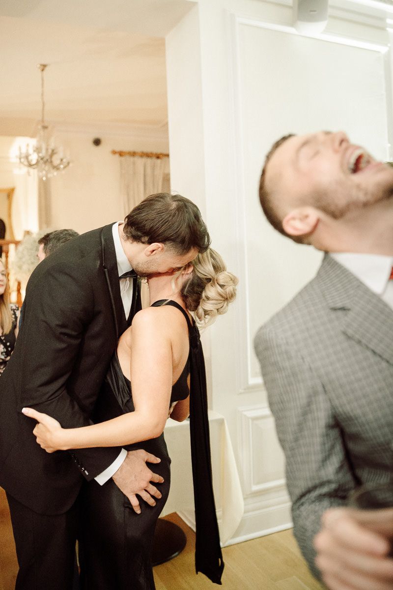 Two couples share candid moments at a formal event, with one pair embracing while another person laughs joyfully.