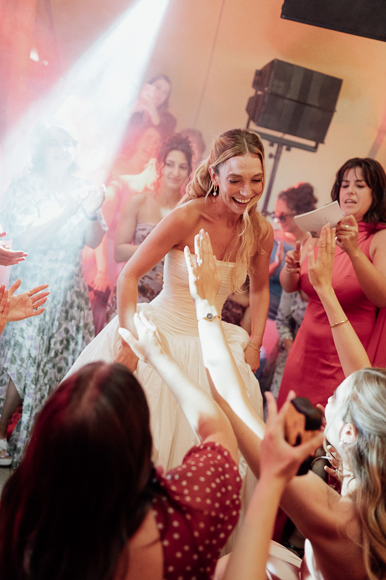 Joyful bride in white gown dancing with guests at wedding reception under bright stage lights.
