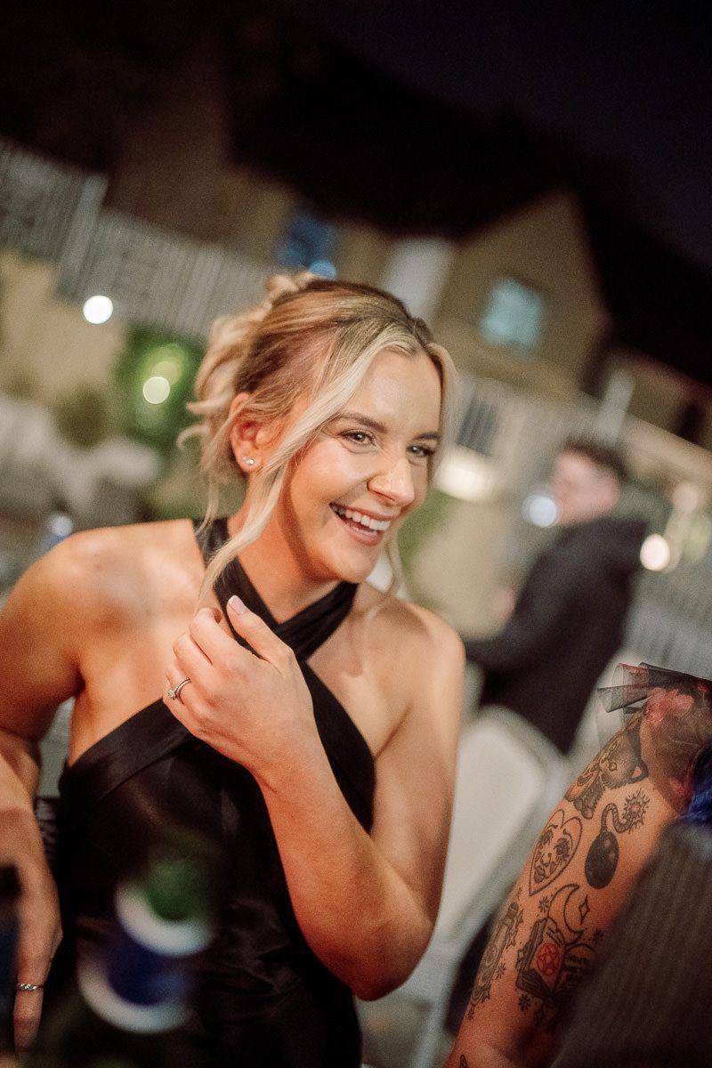 Woman in black dress with visible shoulder tattoo smiling and dancing at an indoor event.