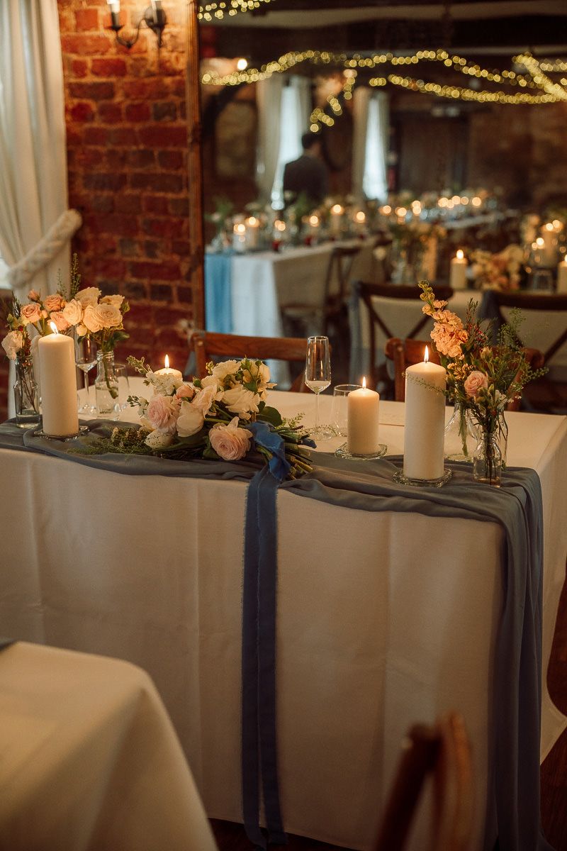 Elegant wedding reception table decorated with candles, roses, and eucalyptus against exposed brick walls.