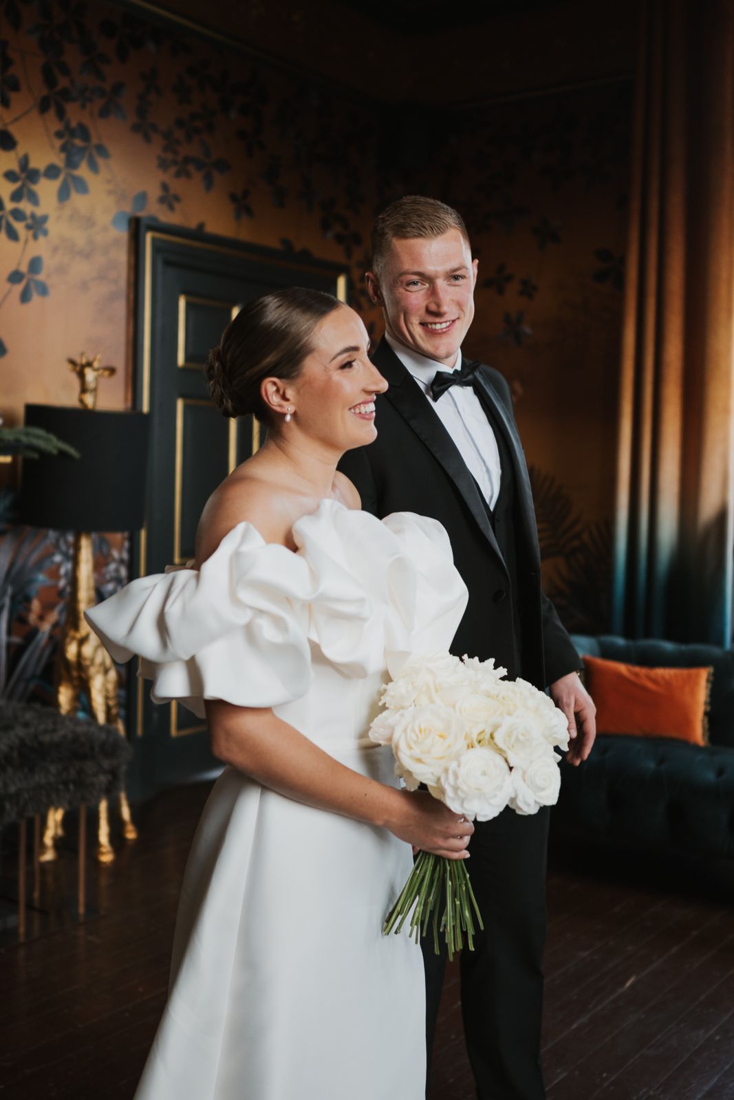 Bride in elegant white wedding gown with dramatic puff sleeves holds classic white bouquet in opulent indoor setting.