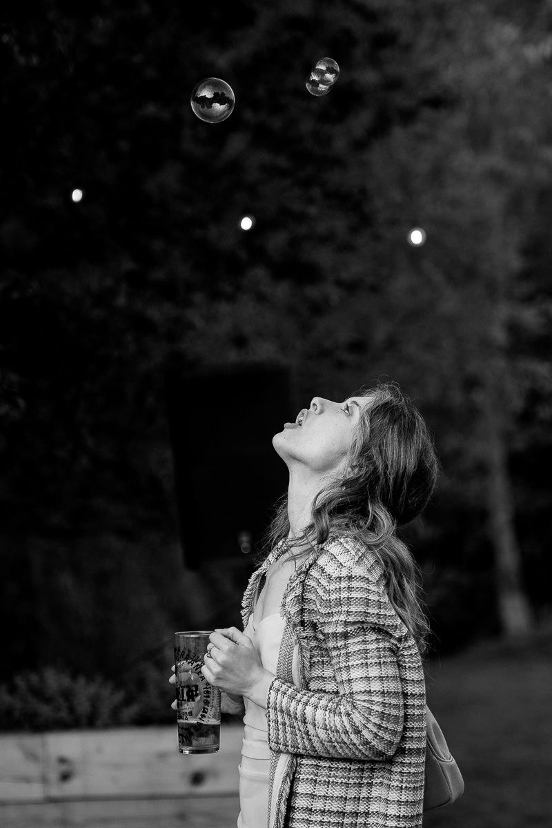 A person in a plaid shirt blows bubbles outdoors in a black and white photograph.