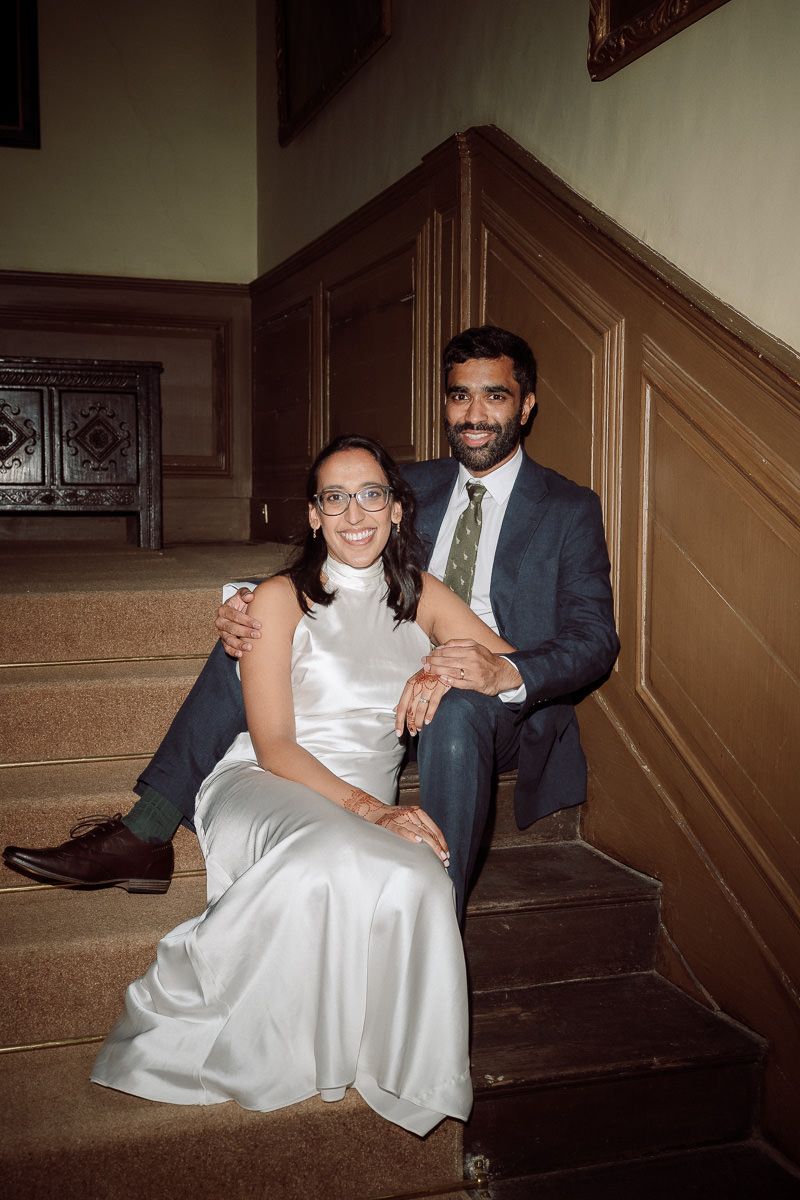 A romantic wedding couple poses on vintage wooden stairs in a dimly lit indoor setting at mapledurham house wedding venue.