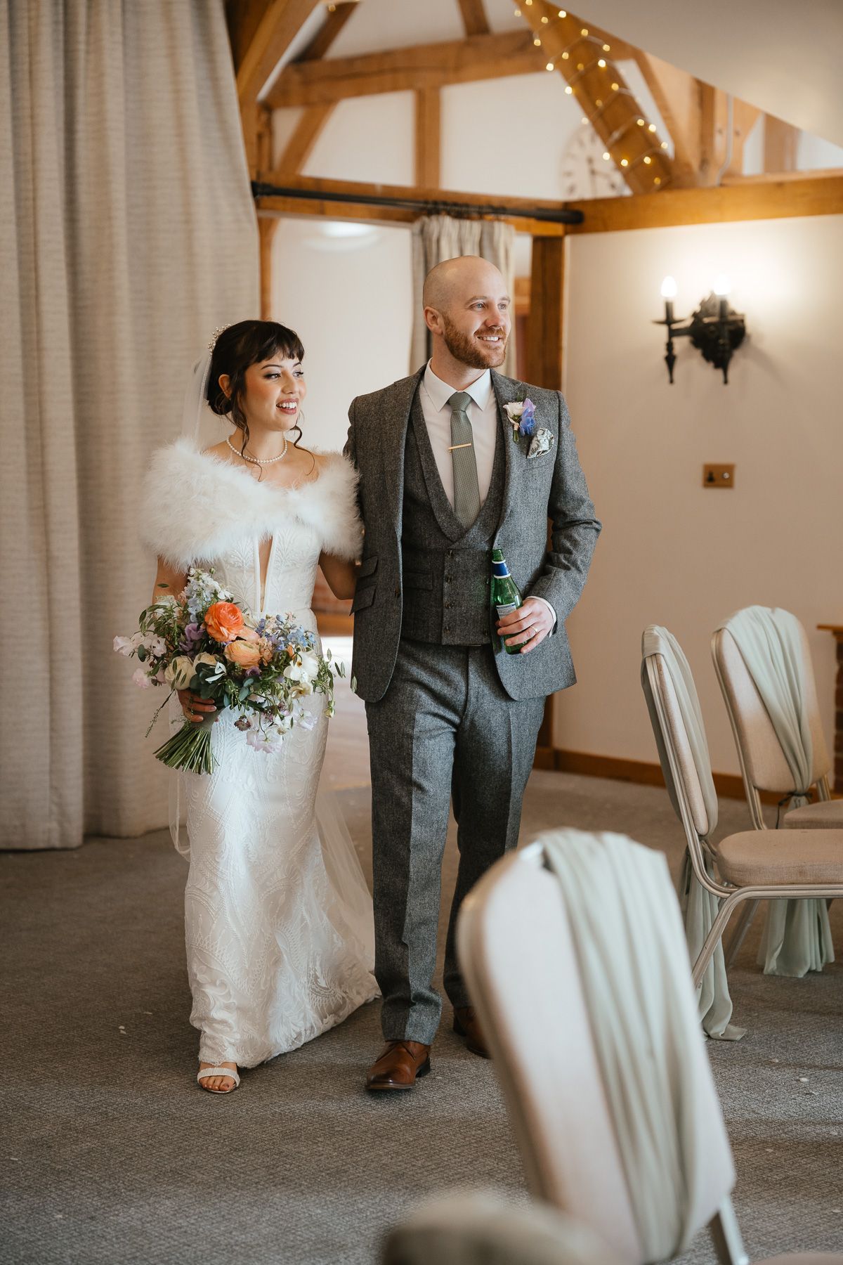 Wedding couple shares a joyful moment in a rustic venue decorated with string lights and wooden beams.