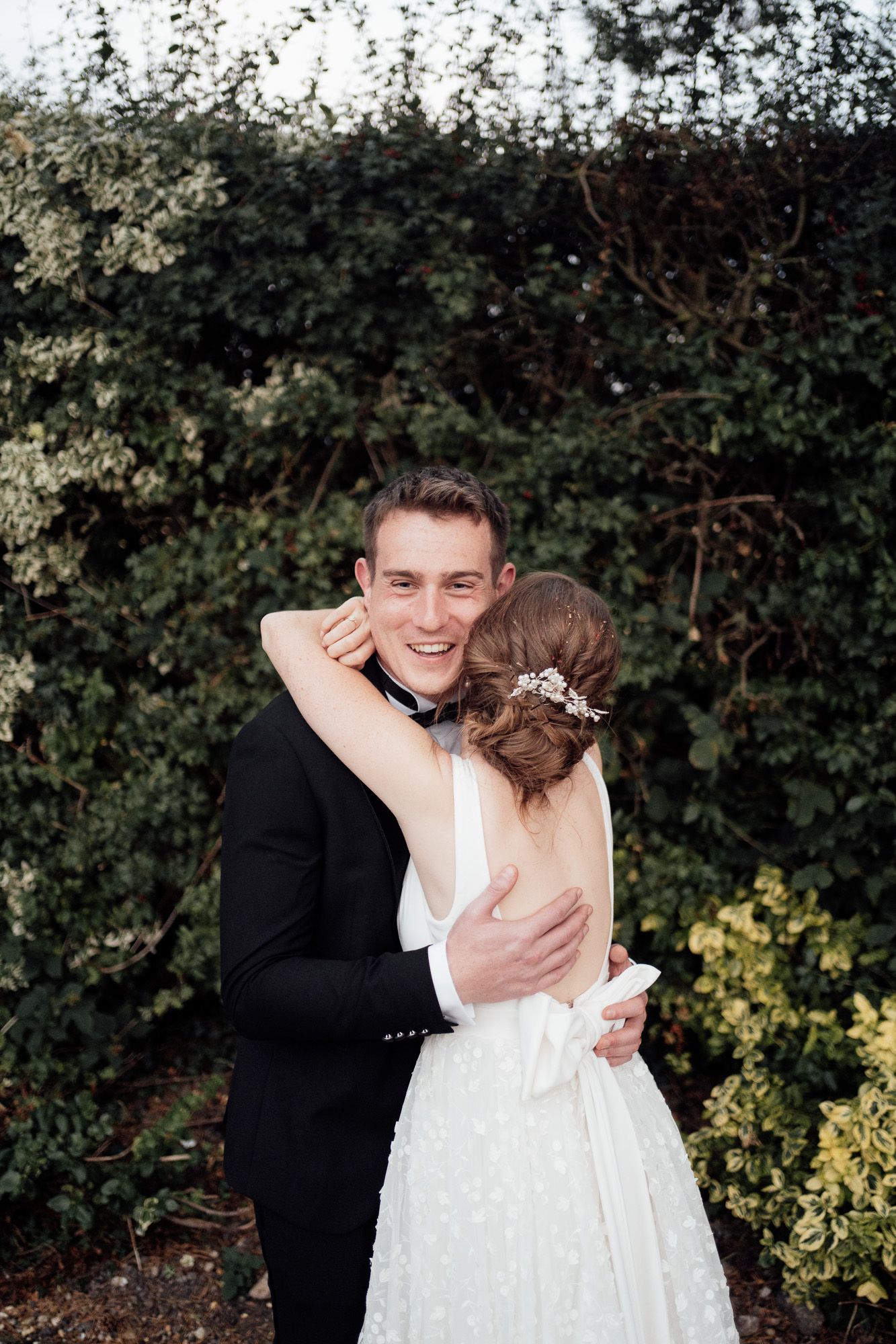 A tender moment between newlyweds embracing outdoors with greenery in the background at a wedding celebration.