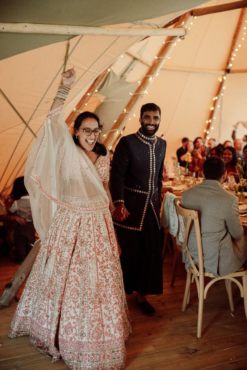 A couple dances together at a wedding reception inside a tent decorated with string lights and rustic decor.