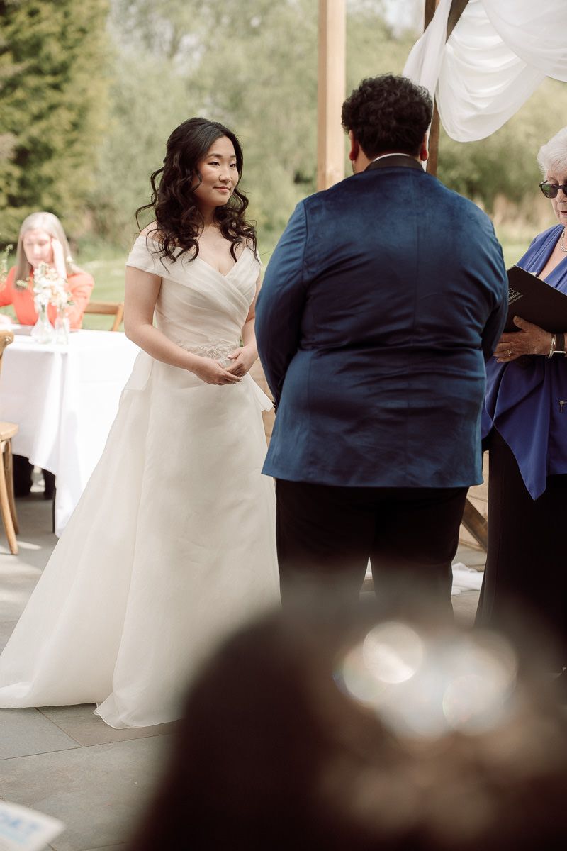 Elegant wedding reception scene with guests gathered around tables under natural lighting.