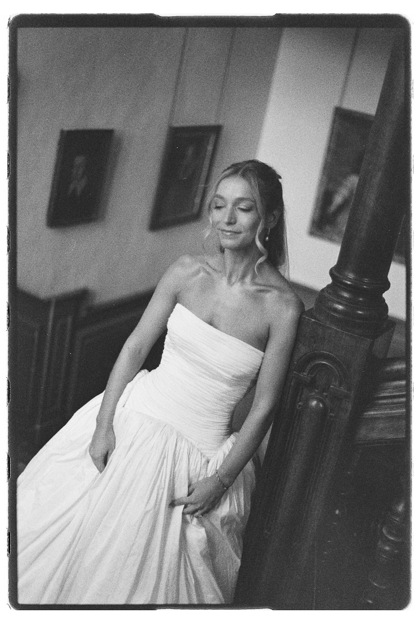 Black and white portrait of bride in strapless white gown leaning on wooden staircase banister.