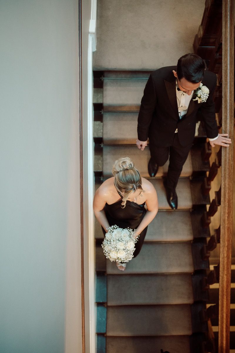 A wedding couple descending wooden stairs, with the bride holding a delicate bouquet of baby's breath flowers.